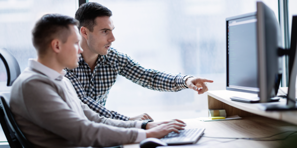 Photo of two people in front of computer discussing what's on screen. One is pointing at the screen