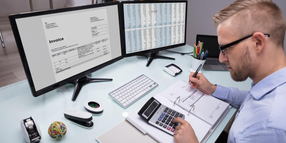 Photo of a person looking at an invoice on a computer desktop while also looking at a calculator